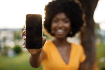 Portrait of a smiling young african woman holding blank screen mobile phone standing in the street