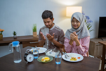 muslim couple wake up early to have sahur or suhur breakfast for fasting. clock at foreground showing the time