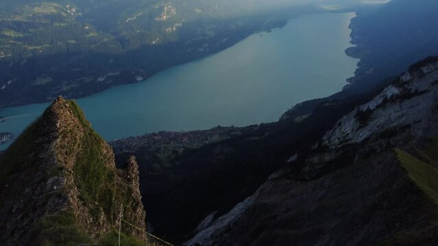 An adventurous hiker standing on top of huge cliff looking at the view of Lake Brienz and the Alps of Switzerland, after a successful hike to the Brienzer Rothorn