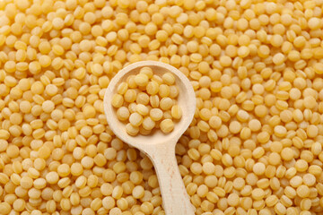 Wooden spoon on uncooked ptitim background, close up