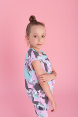 An expressive charming little girl in a bright suit stands on a pink background in the studio
