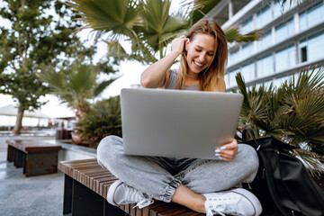 Young beautiful casual woman working on a laptop sitting on the bench in the street