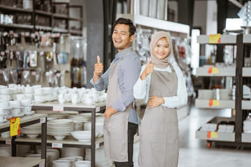 Shop assistant boy and girl in veil smiling with thumbs up in houseware store