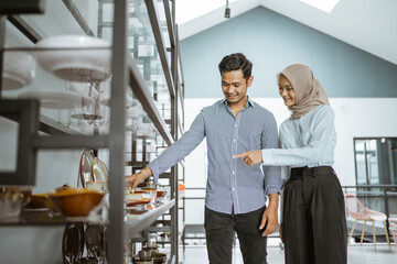 Muslim couple looking at ceramic cups on shelf in houseware store