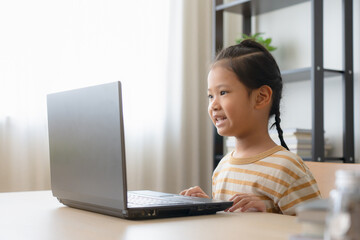 Asian school girl studying online class on laptop. Happy kid enjoy learning from home using laptop in a living room.
