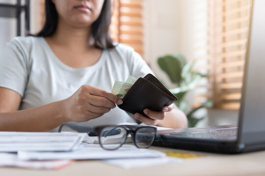 Worried Asian woman has less money in wallet. Bills waiting to be paid with few cash during crisis unemployed concept.