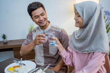 muslim couple wake up early to have sahur or suhur breakfast for fasting. clock at foreground showing the time