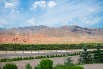 Mountain gorge with red ridges, trees and road. Landscape of Kyrgyzstan. Copy space