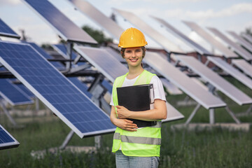 Large smiling ecological engineer woman posing in the middle of photovoltaic solar panels farm...