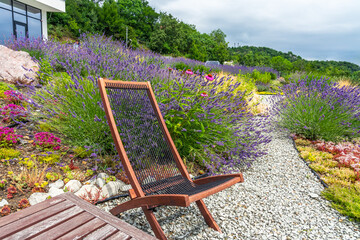 Wooden armchair among lavender flowers on Alpine hill and stone path near the house