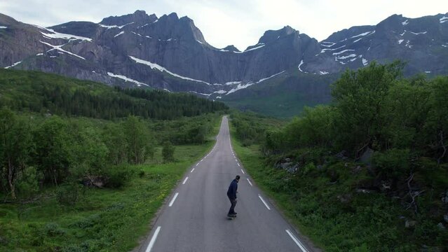 Skater enjoying the scenic view on a empty road in Lofoten during midnight sun in Norway, forwarding shot
