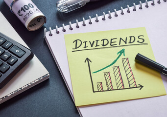 Sticky note with text Dividends and hand drawn increasing profit bar chart on desk. Business...