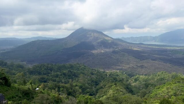 A beautiful static view of volcano with a cloud cap behind green forests and hills. Peaceful natural background for design. Misty highlands of Bali island.