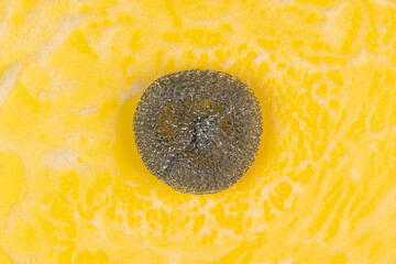 Stainless steel scrubber with foam on a yellow background.