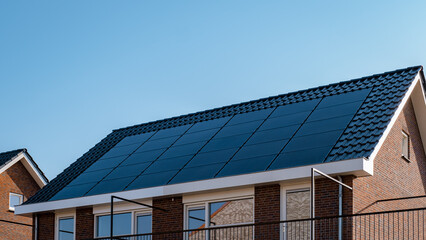 Newly build houses with solar panels attached on the roof against a sunny sky Close up of a new building with black solar panels. Zonnepanelen, Zonne energie, Translation: Solar panel, , Sun Energy.  © Fokke Baarssen