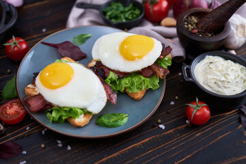 Fried eggs, bacon and cream cheese sandwiches on a plate on wooden table at domestic kitchen