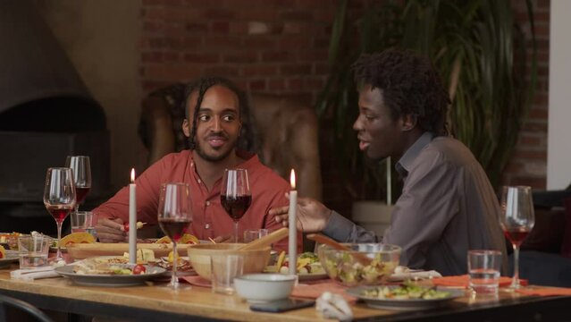 Waist up slowmo of two young African American men sitting at festively decorated dinner table having conversation