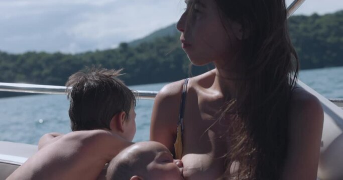Mother breastfeeds baby girl on boat in beautiful tropical location