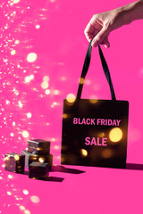 Black friday cocnept. Gift boxes and hand holding shopping bag on violet background with gold bokeh and sparles