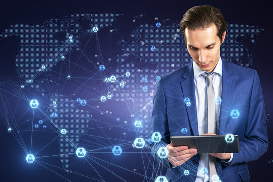 Attractive young european businessman using tablet with abstract glowing digital map and connections on blue background. Communication and network concept.