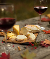 Autumn picnic with bread, cheese and glasses red wine on wooden table with maple leaves. Romantic dinner in garden in evening outdoors. Still life