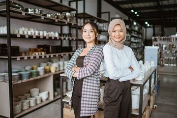 Two beautiful asian girls smiling while standing back to back with arms crossed in houseware store