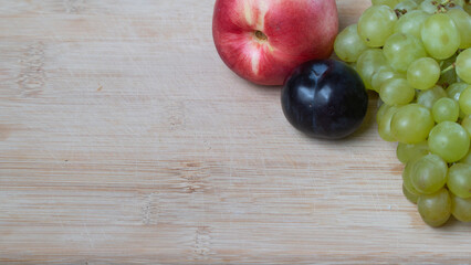 A bunch of grapes, plums and nectarine on a wooden background with a place under the text