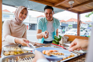 muslim couple ordering food to break fasting in traditional food market stall served by the seller