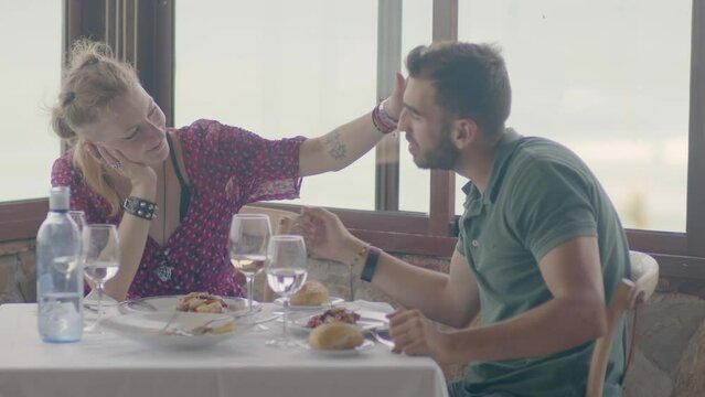4K SlowMo - Young couple (20-25 years old) having a date in a restaurant gazebo overlooking the beach - cuddling, eating assorted raw tuna, drinking wine, toasting