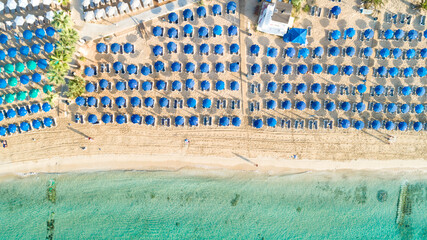Aerial above bird's eye view of Pantachou - Limanaki organised beach (Kaliva), Ayia Napa, Famagusta, Cyprus. Blue aligned umbrellas, golden sand, parasols, sunbathing sea beds clean turquoise water