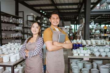 Two shop owners in apron holding digital tablet standing back to back in houseware store