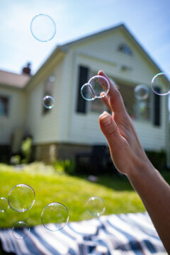 dreamy image of child's hand reaching towards blowing bubbles in suburban yard at picnic