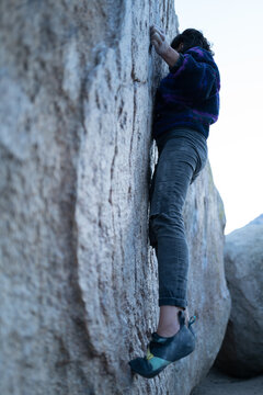 Rock climber intensely crimps granite hold in Buttermilk boulders, Bishop, CA