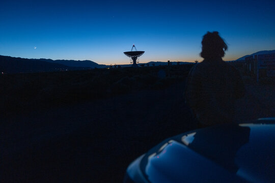 Curious stargazer and astronomy buff ponders of life meaning near radio observatory under dark night sky