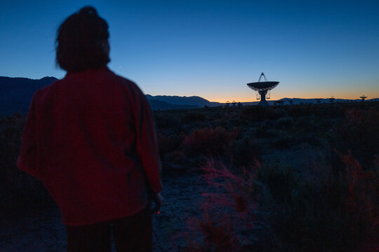 Curious stargazer and astronomy buff ponders alien life in moody red light near radio observatory under dark sky