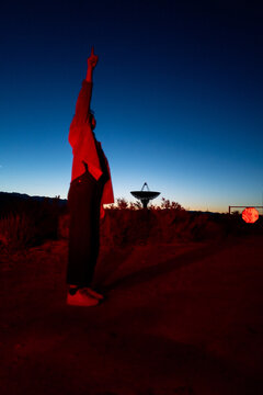 Curious stargazer and astronomy buff ponders alien life in moody red light explores radio observatory in dark sky