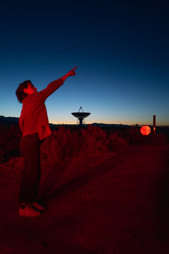 recreational stargazer and astronomy buff ponders alien life in moody red light near radio observatory in dark sky