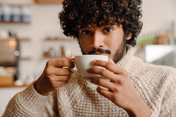 Young handsome indian curly indian man drinking coffee at cafe