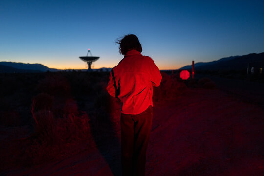 Curious stargazer, alien, and astronomy buff in moody red light explores radio observatory at night