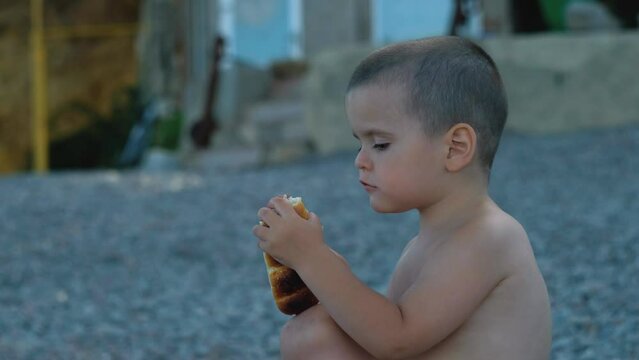 Little Boy Eating A Bun On The Beach