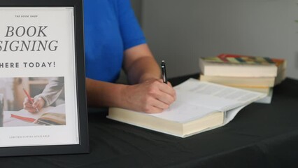 Female author signing a book autograph at a table at a book launch.