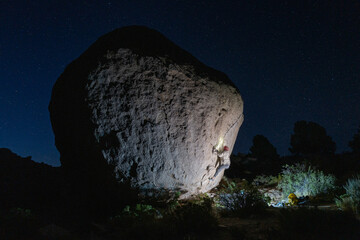 Epic shot of rock climber on highball boulder under starry night sky on "Cover me with Flowers" route in Buttermilks, Bishop, CA