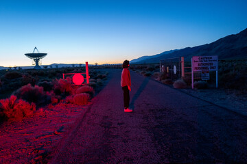 Curious stargazer and astronomy buff ponders alien life in film noir red light near radio observatory under dark sky