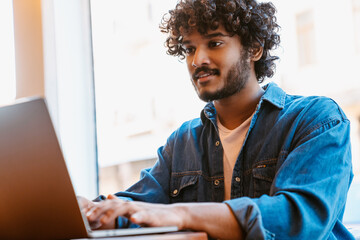 Young calm handsome indian curly man working with laptop