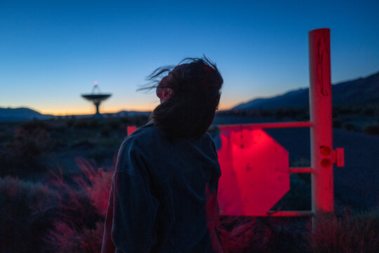Curious stargazer and astronomy buff ponders alien life in moody red light near radio observatory under dark sky