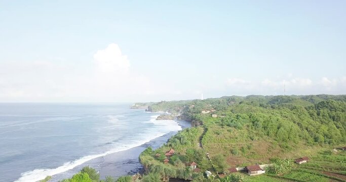 drone flight over the south beach of java island indonesia when the first sun rays hit the green coastal mountains in the morning