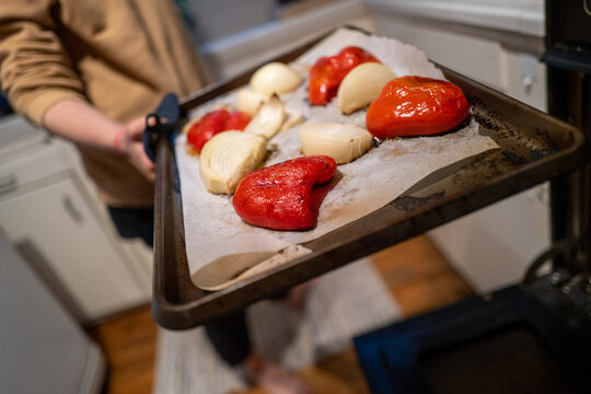 home cook holding tray of fresh roasted red peppers and onions