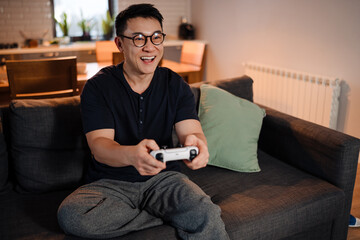 Adult happy smiling asian man sitting on sofa and playing