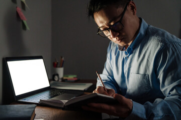 Adult focused asian man taking notes to the notebook