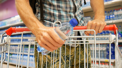 Close-up of a shopping trolley in a supermarket and a man puts a bottle of water into it